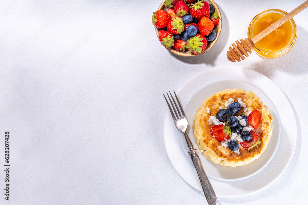 Sweet homemade cottage cheese pancakes, american version of syrniki or cottage cheese fritters, big pan fried cheesy pancakes with fresh summer blueberry and strawberry, healthy high-protein breakfast