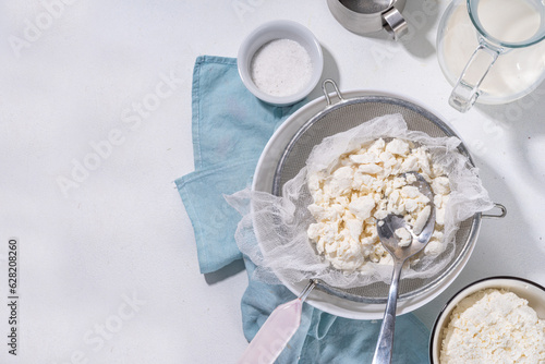 Making cottage cheese, homemade fermenting dairy product. Homemade cottage cheese in cheesecloth bags on kitchen table, woman hands drain cheese at home top view copy space
