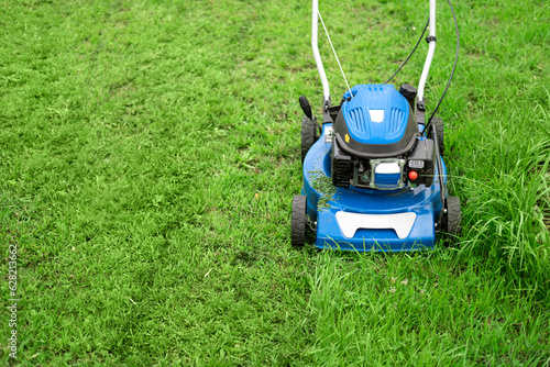 Lawn mower cutting grass. Small grass cuttings fly out of lawnmower. Grass clippings get spewed out of a mower pushed around by landscaper. CloseUp. Gardener working with mower machine. Mowing lawns