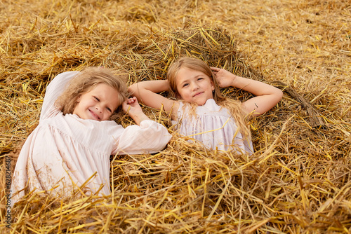 two blonde girls with long hair in linen dresses lie in a haystack on a mown field © Тамара Киреева