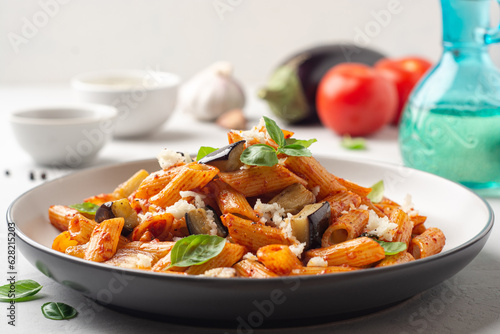 Pasta alla Norma. Traditional Italian dish with eggplant, tomato sauce, ricotta cheese and basil in plate on concrete background