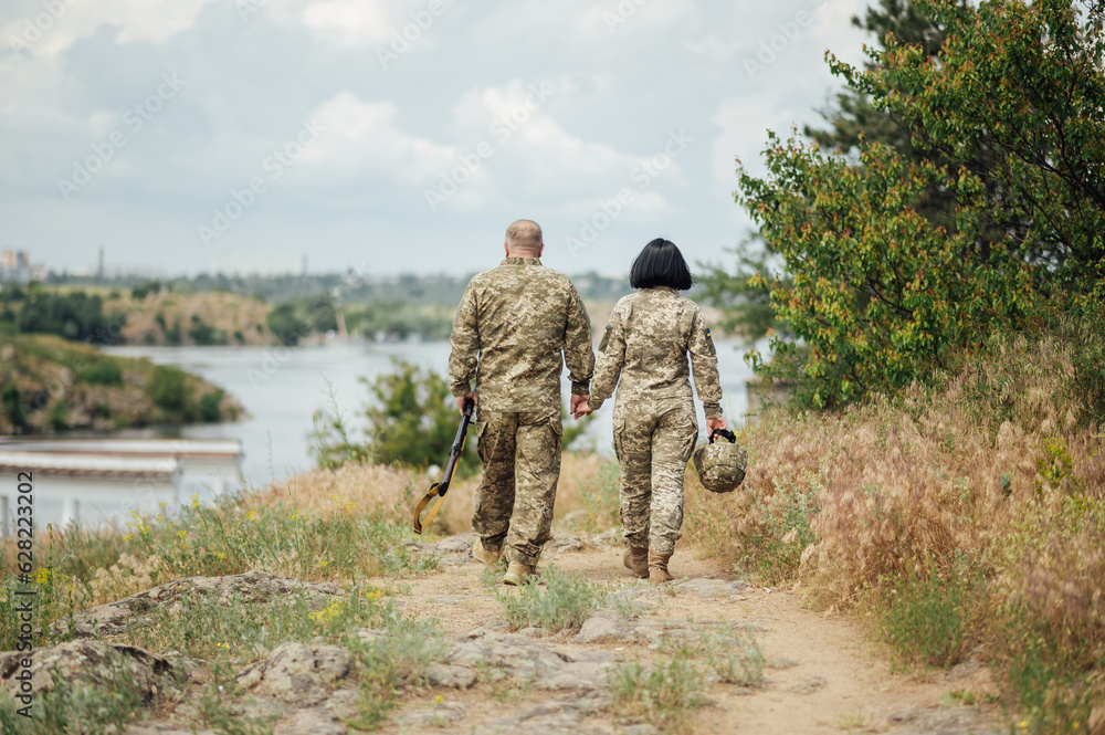 A man and a woman in the military uniform of Ukraine walk along the path and hold hands. A man and a woman in the military uniform of Ukraine walk along the path and hold hands.