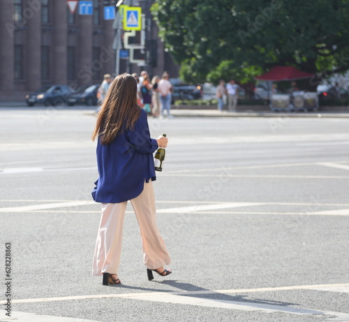 A young woman with an open bottle of sparkling wine in her hand walks down the street, St. Isaac's Square, St. Petersburg, Russia, July 13, 2023 © Станислав Вершинин
