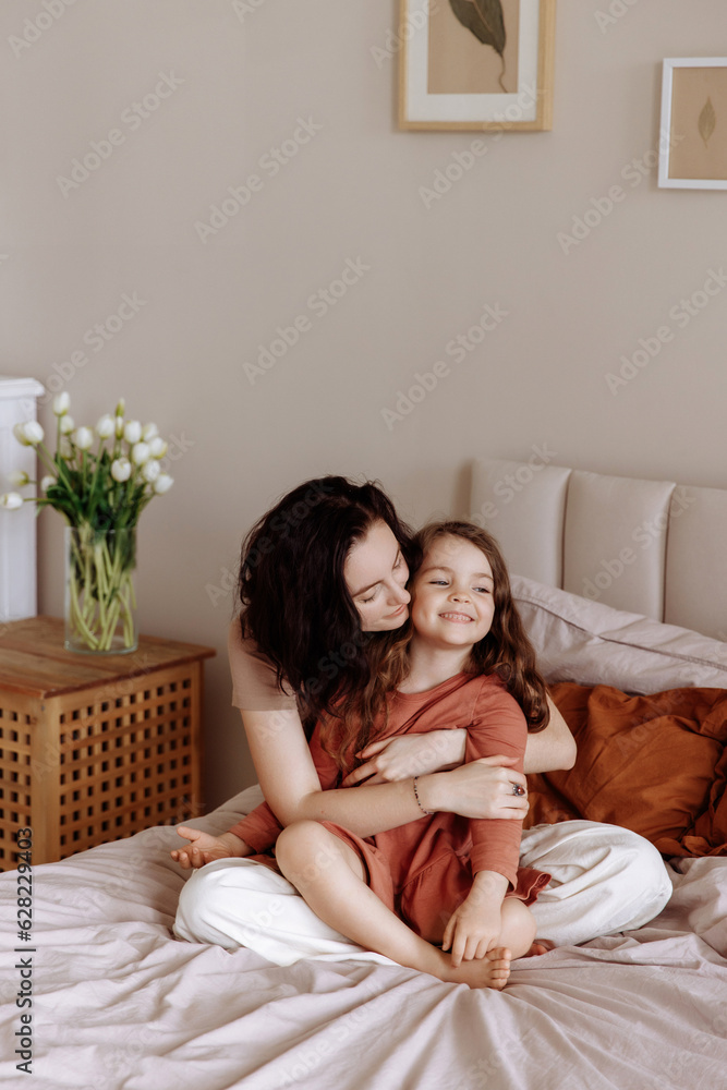 Happy loving family. Mother and her daughter girl play and hug while lying on the bed in a cozy bedroom. Happy loving family. Mother and her daughter girl play and hug while lying on the bed in a cozy bedroom.