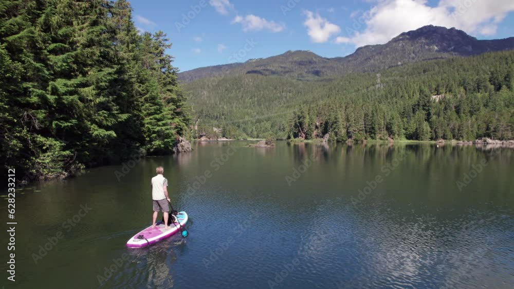 Man paddle boarding on a pristine mountain lake on sunny day with his dog, stand up paddle, mountains, Whistler, BC, water sport. 4K 24FPS Man paddle boarding on a pristine mountain lake on sunny day with his dog, stand up paddle, mountains, Whistler, BC, water sport. 4K 24FPS