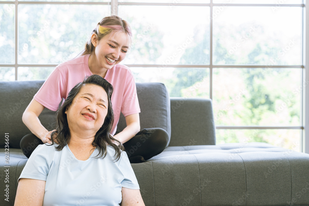 Fototapeta premium Asian mother fill happy that Cute Asian daughter sit on sofa and giving massages shoulder, relieves pain of elderly Asian mother at home.