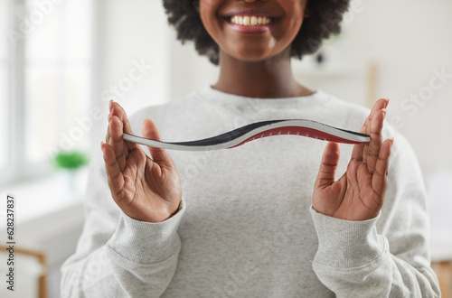 Cropped shot of a happy, smiling young African American woman holding an orthotic orthopedic arch support shoe insole in her hands. Soles, footwear, feet health concept photo