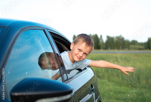 Happy boy rides in car, looks out of window and dreams. Kid catches wind with window open in car. Happy holidays, road trip