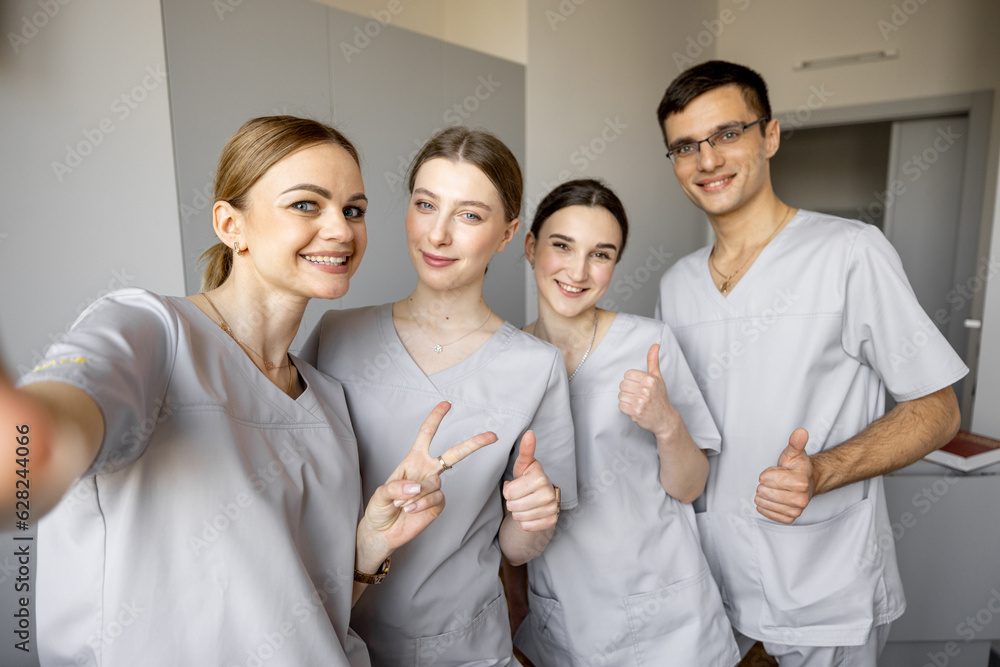 Young team of nurses making selfie photo, while standing together in medical ward. Portrait of cheerful nurses in clinic Young team of nurses making selfie photo, while standing together in medical ward. Portrait of cheerful nurses in clinic
