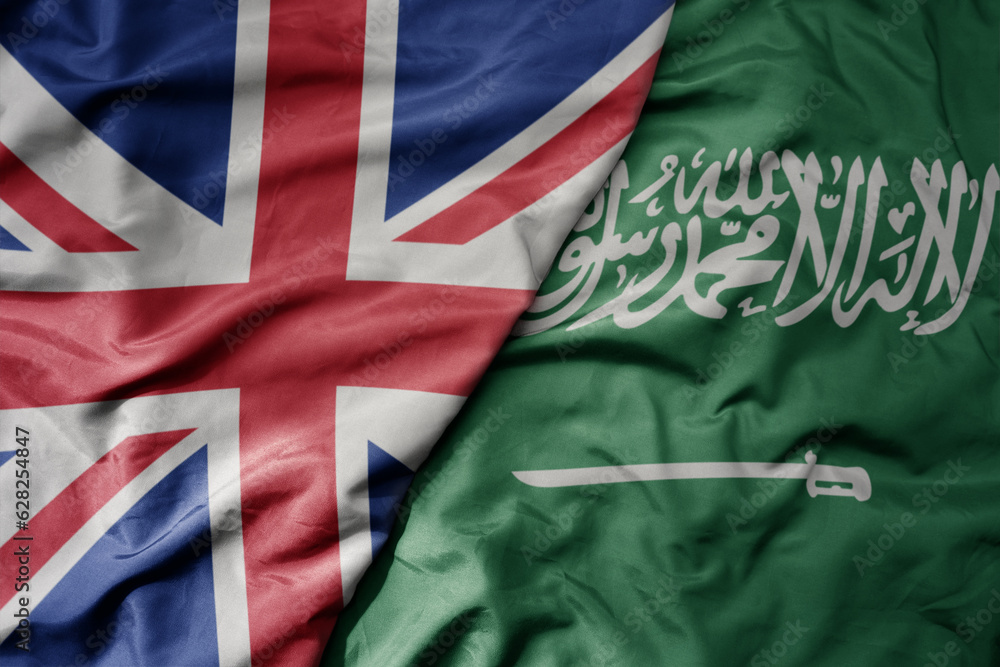 Fototapeta premium big waving national colorful flag of great britain and national flag of saudi arabia .