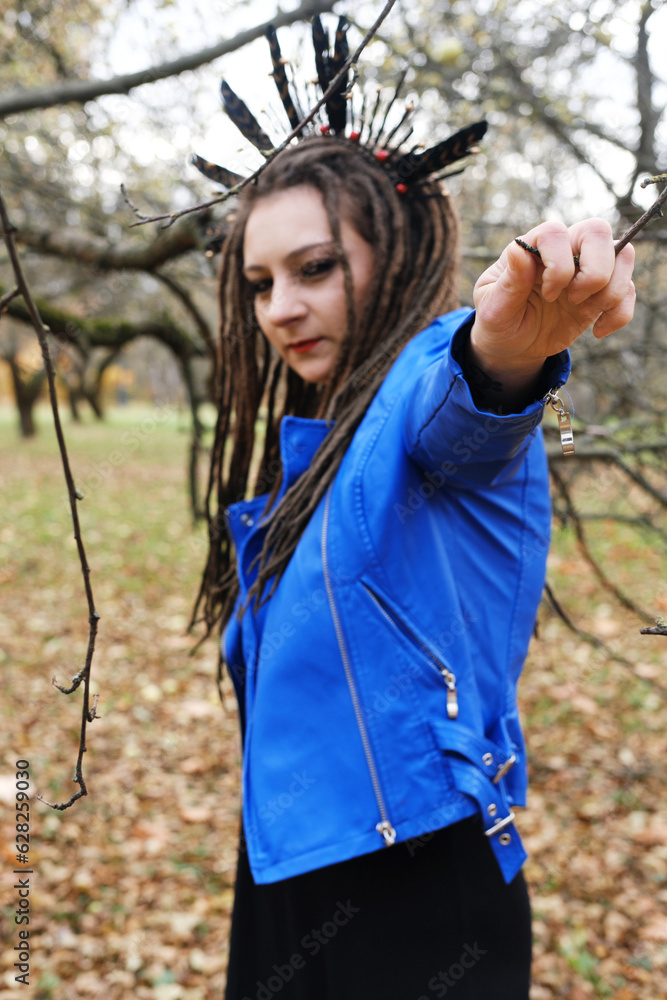 Naklejka premium Portrait of a Woman in a blue leather jacket with dreadlocks and a headband with feathers. Woman posing in autumn park and looking at camera
