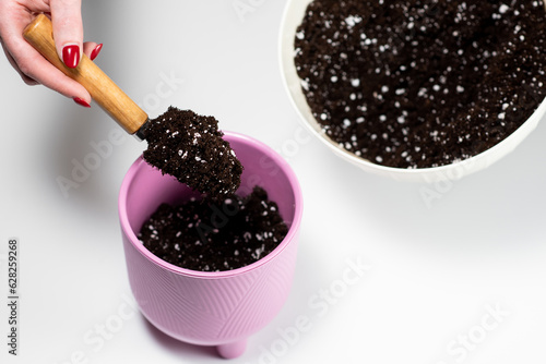 Girl pours soil mixed with perlite into a pink flower pot with a spatula before transplanting a houseplant. Transplanting indoor flowers