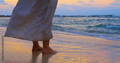 Waves washing over feet and wind blows woman dress who is standing on shore at epic sunset. Calm and chill atmosphere is best way to refresh your mind. Let waves wash over your feet in calm atmosphere © ShantiMedia