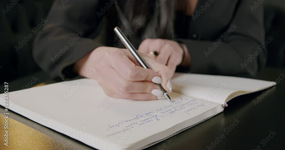 Businesswoman writing by hand or making a to-do list in paper planner and managing work tasks. Close-up image of a woman's hands writing down and planning all her tasks in a workbook Businesswoman writing by hand or making a to-do list in paper planner and managing work tasks. Close-up image of a woman's hands writing down and planning all her tasks in a workbook