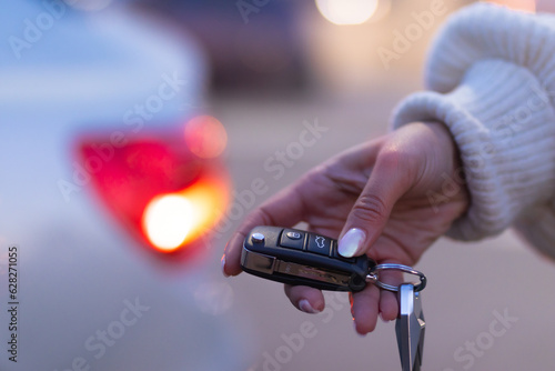 Hand of young woman holding the keys of her first car. Active auto backlight. Concept rent a car.
