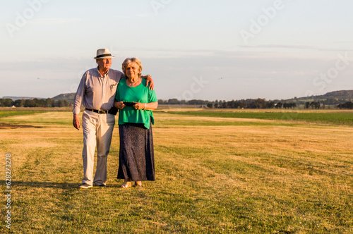 An older couple walking through a field, with the evening sunlight hitting their faces.