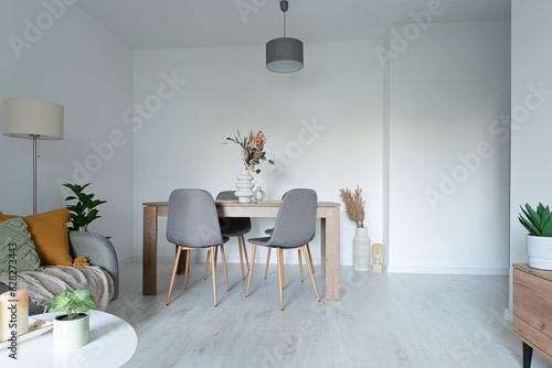 Living room with table and chairs in modern interior. Stylish apartment with white wall, sofa and wooden floor.