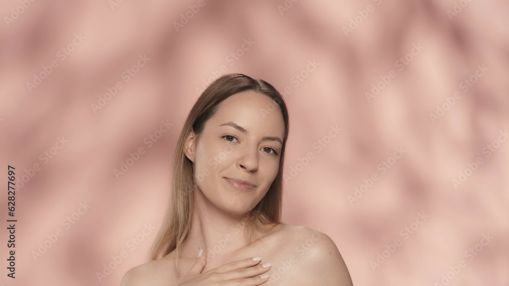Naklejka premium A young woman enjoys her perfect smooth, delicate skin. Portrait of a smiling seminude woman, isolated on a pink background close up. The concept of beauty, cosmetology, skin care, spa.