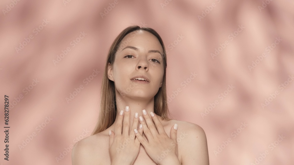 A young woman enjoys her perfectly smooth, delicate skin, touching her neck with both hands. Portrait of a smiling seminude woman, isolated on a pink background close up. A young woman enjoys her perfectly smooth, delicate skin, touching her neck with both hands. Portrait of a smiling seminude woman, isolated on a pink background close up.