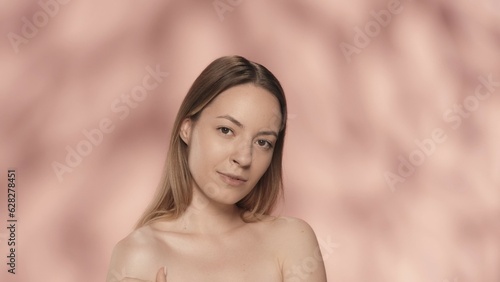 Portrait of a seminude woman on a pink background close up. A woman with natural makeup looks straight ahead. Beauty concept. Natural beauty, cosmetology, skin care.