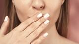 The woman raised her delicately manicured hand to her mouth for an air kiss. Woman's hand covering her mouth close up on a blurred pink background.