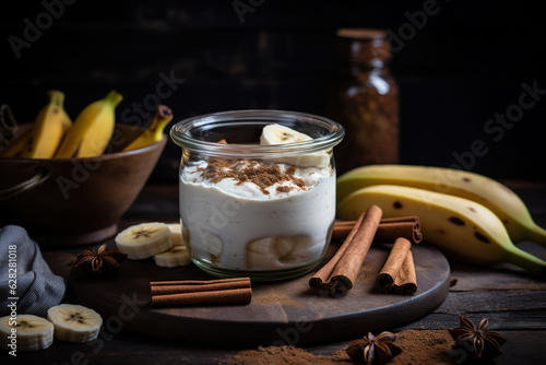 Tasty yogurt with banana slices with cinnamon powder and cinnamon sticks. Jar with healthy banana smoothie with yogurt and cinnamon. Nutritious and healthy yogurt breakfast. Generative AI