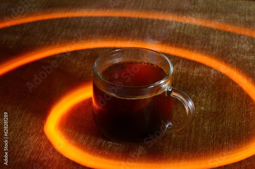 A floating transparent glass of coffee on a brown background with light orange concentric spirals in circles around the glass. Long exposure photo