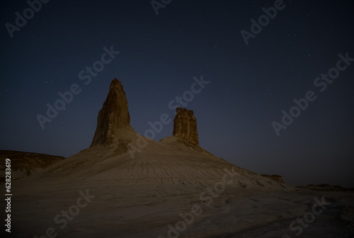 Chalk and limestone remnants in the Kazakh steppe at night against the background of the starry sky and the moon, vertical landforms after weathering in the desert