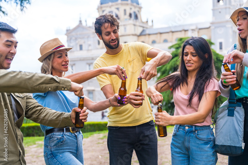 Multi-ethnic group of friends partying in a city park with beers. opening the bottles