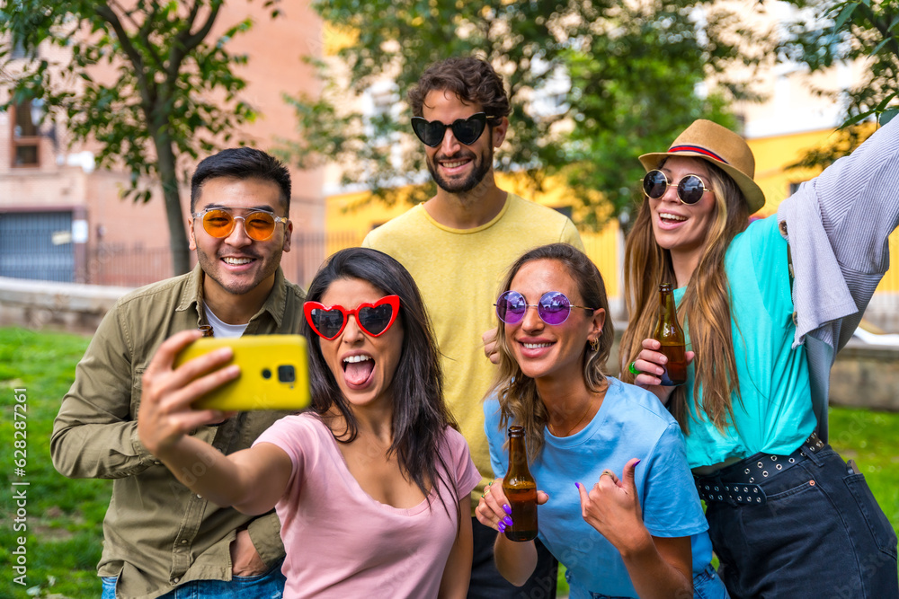 Obraz premium Multi ethnic group of friends partying in the city park taking a selfie, friendship and fun concept with sunglasses