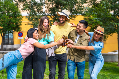 Multi-ethnic group of friends partying in a city park toasting bottles of beers