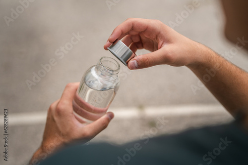 close up hands unknown caucasian man open plastic bottle of water