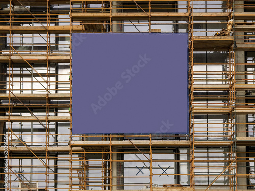 Side of a new building in scaffolding and safety nets and blue color banner. Construction site safety measures. Developing commercial or residential property. Growth concept.
