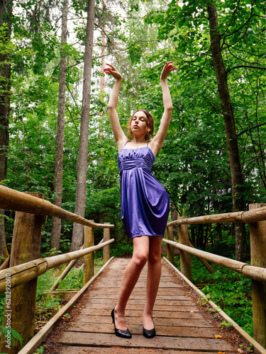 Teenager girl in elegant blue dress posing in a park during senior photo session. Fashion and glamour concept. Young lady model with slim body type. Beauty and style theme.