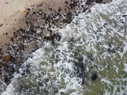 Beautiful sea waves crashing against the sandy beach with stines. 