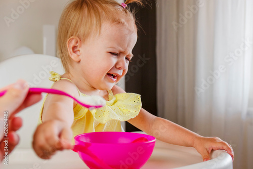 Photography Toddler girl sitting in high chair rejecting eating porridge