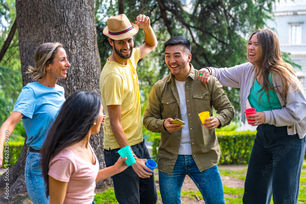 Multiethnic group of birthday party in the city park dancing and smiling together with trees and nature