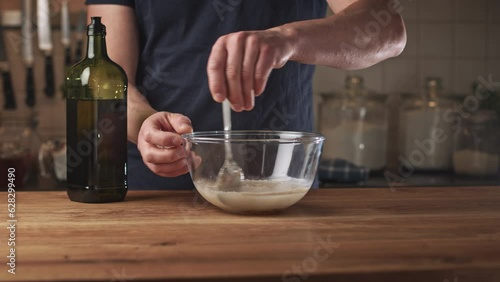 Home chef mixing dry yeast with water in a glass mixing bowl.
