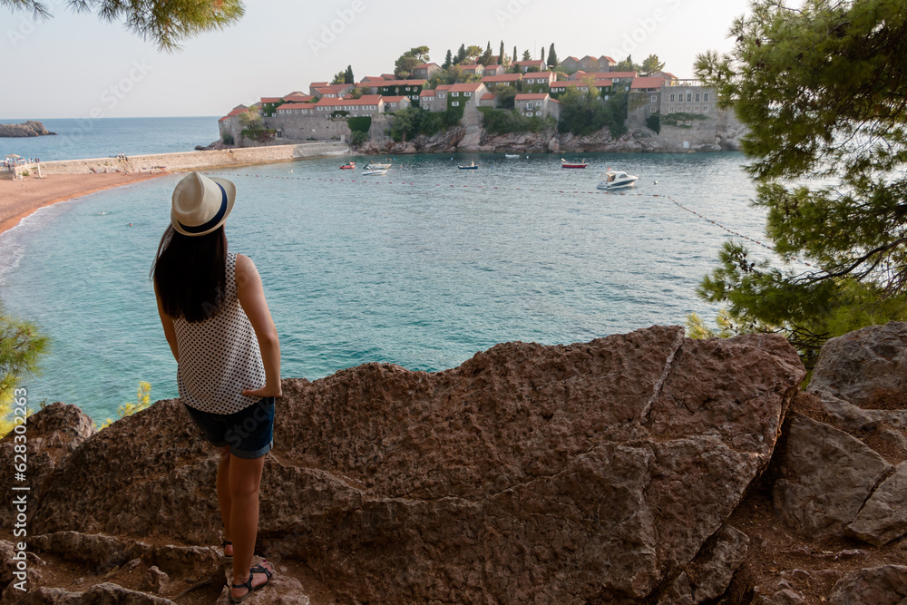 girl tourist in a hat looks from a cliff on the island of Sveti Stefan in Montenegro