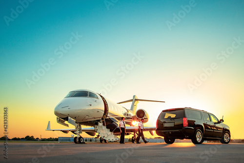 Two Pilots approaching SUV to greet guest and to assist boarding Jet on tarmac of small airport at sunset photo