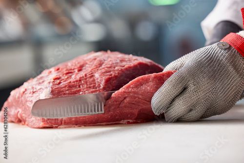 Detail of butcher slicing through side of beef, behind counter of meat market of grocery store 
