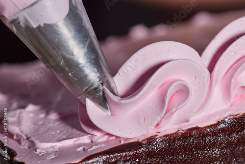 Close up detail of piping bag adding strawberry frosting accents to chocolate layer cake photo