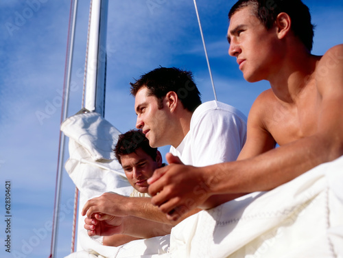 Three young male crew members leaning on the sail and boom catching up 