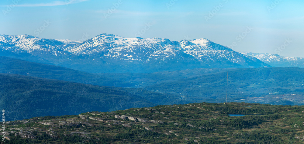 Panorama over nordic mountain peaks in Norway from a hike up Hauknestinden, Hauknes, Mo i Rana, Helgeland, Norway. Peaks in a fjord landscape, snow covered. Clear Norwegian summer skies. Wild Norway