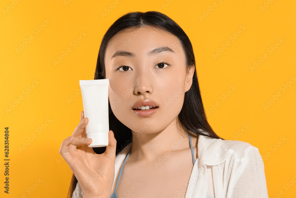Beautiful young woman holding sun protection cream on orange background Beautiful young woman holding sun protection cream on orange background