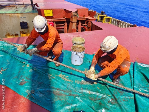 Crews or seaman are lubricating or greasing Hoisting wire of deck crane during renewal operation.