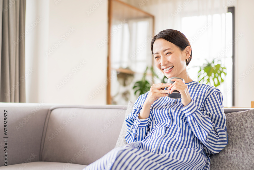 リビングでソファーに座りくつろぐ日本人ミドル女性/飲み物を飲む リビングでソファーに座りくつろぐ日本人ミドル女性/飲み物を飲む