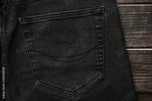 Black jeans with pocket on wooden background, top view
