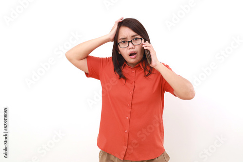 Shocked asian woman holding her head while talking on the phone. Isolated on white