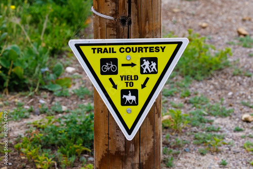 Photography Triangular yellow trail courtesy sign on a wood post giving yield instructions